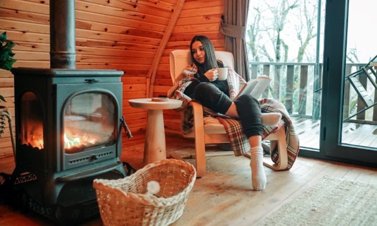 A woman curls up by a wood-burning fireplace