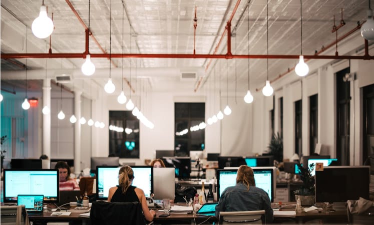 Several people sit side-by-side at computer stations in a large room.