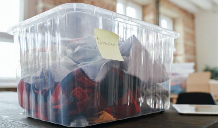 A clear plastic bin with a light yellow post-it note that reads “Donation.” It’s almost full of clothing to be donated.