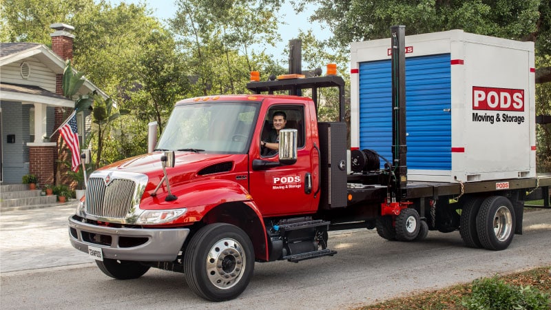 A PODS truck driver transports a PODS portable storage container through a residential neighborhood