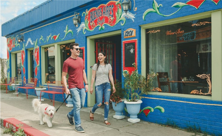 A happy couple walks their dog beside a colorful restaurant in Austin, Texas.