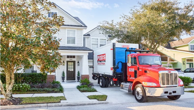 A PODS truck delivering a portable moving container to the driveway of a new home
