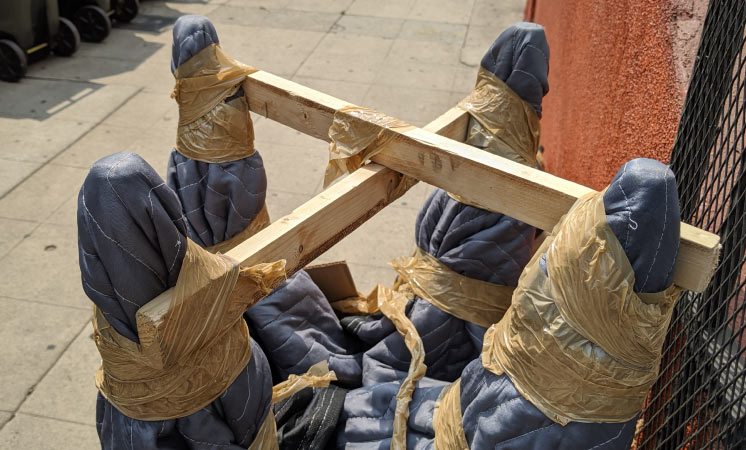 A chair wrapped in a moving blanket with its legs braced with wooden boards and tape to protect it from damage during long-term storage.