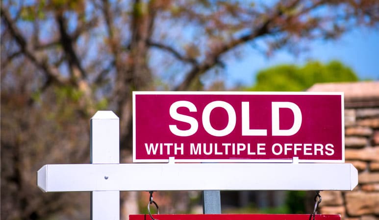 A real estate sign with a placard reading "SOLD WITH MULTIPLE OFFERS" on top