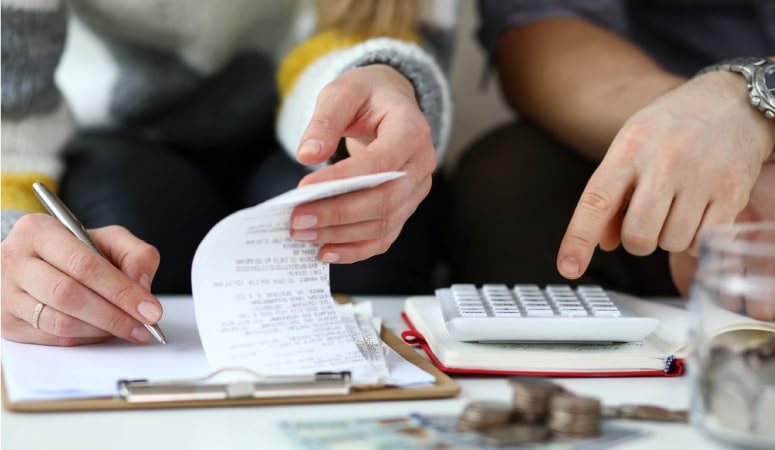 A shot of a couple's hands working on expense forms, using a pen and paper and a calculator