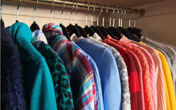 Clothing hung up in a closet and organized by color
