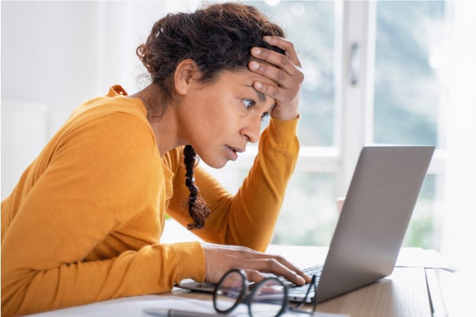 A stressed woman is looking at her high water bill online. Her head is in her hands because the price has increased.