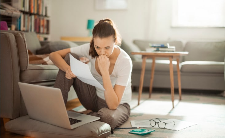 A young woman sitting in the living room of her apartment, reviewing her lease, and researching breaking her lease online