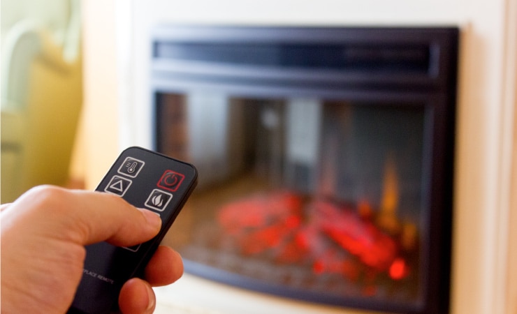 A man uses a remote to control the temperature of his electric fireplace