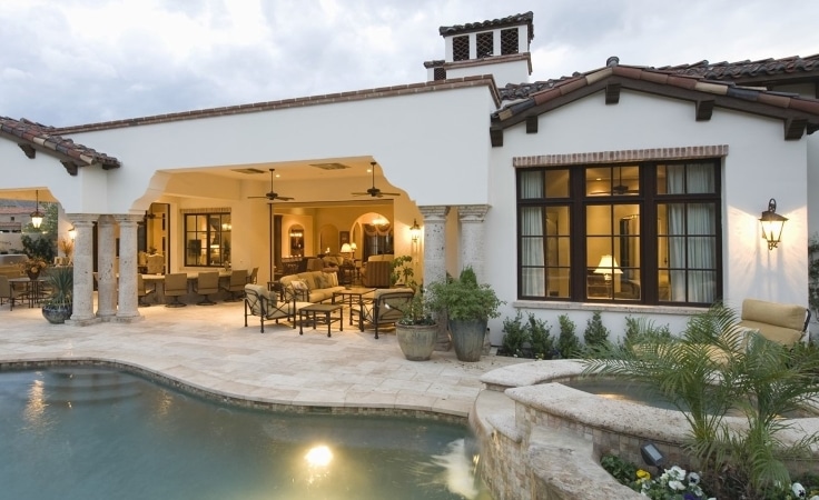 The back patio of a beautiful home in San Diego at dusk. The pool water is still and the outdoor furniture is welcoming under the warm yellow of the nearby fixtures.