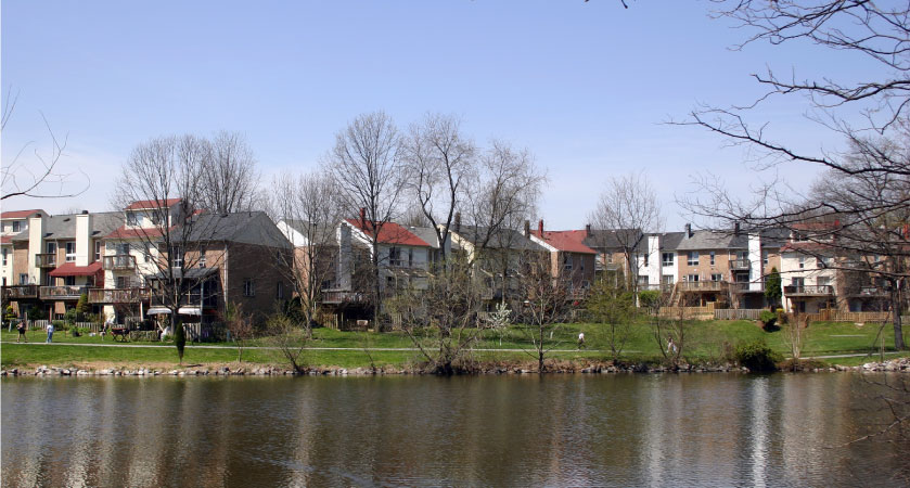 The rear view of residential buildings that share a large greenspace and a lake with a walking trail in Columbia, Maryland.