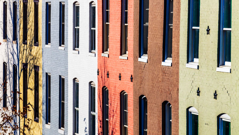 A beautiful array of colored brick row houses, typically seen in the Baltimore area. Distinct colors are used for each home, including yellow, blue, white, red, brown, and gray.