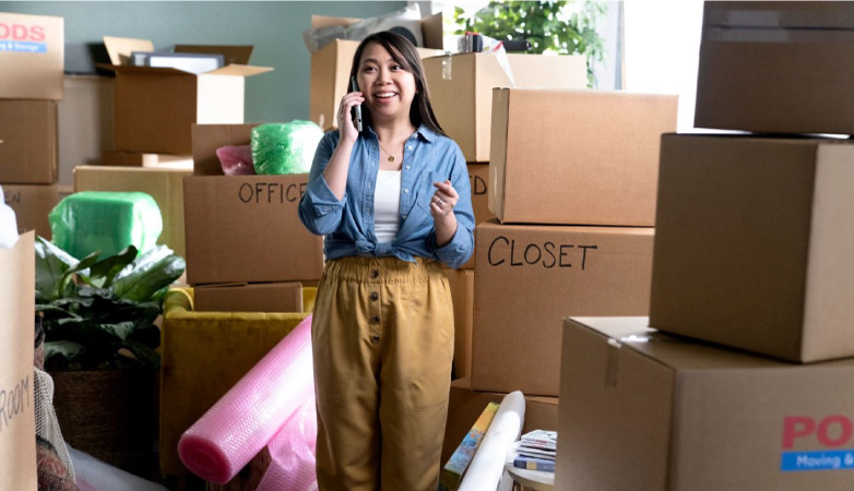 A woman is talking excitedly on the phone while surrounded by stacks of moving boxes in her home.