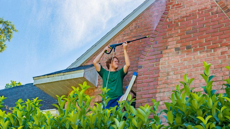 a man pressure washing the outside of his brick house