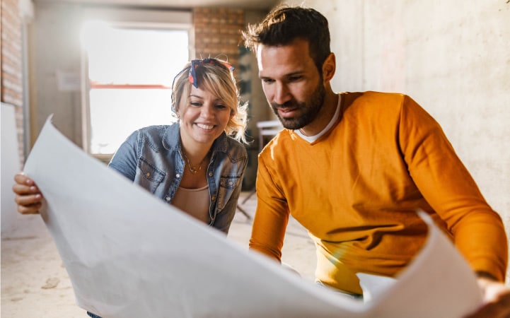 A man and woman review blueprints as they renovate their home