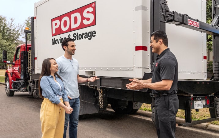 A couple speaking with a PODS driver in front of his truck and a PODS moving and storage container