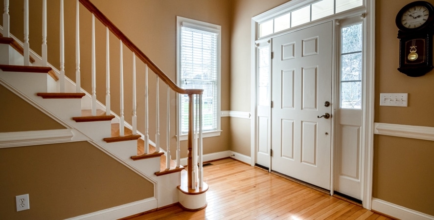 An entryway to a single-family home with a staircase and lots of natural lighting.

