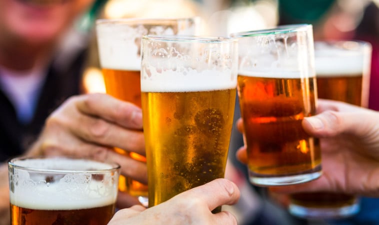 Friends clink their glasses together while enjoying craft beers on a night out.