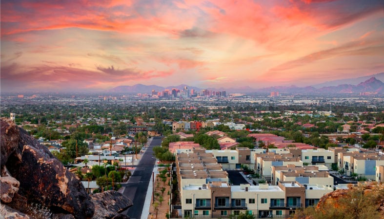 Residential buildings with downtown Phoenix in the background under a colorful sunset sky.