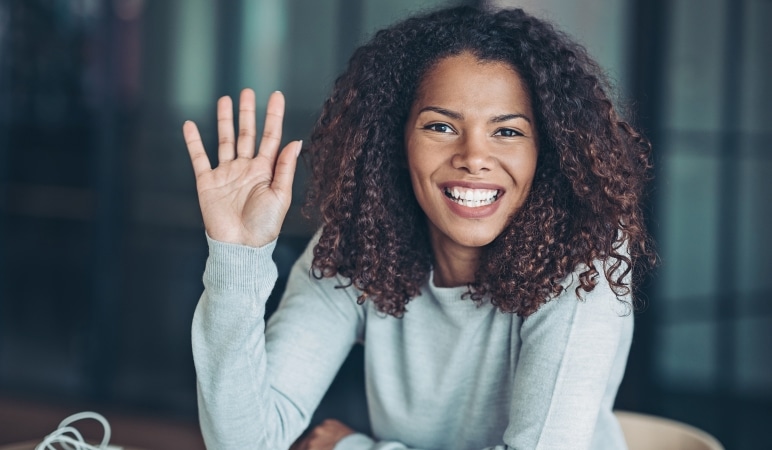 A young woman is smiling while she raises her hand to ask a question.