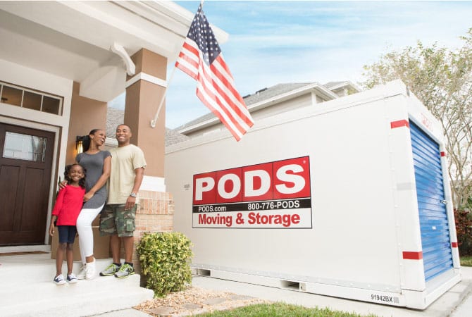 A happy military family is standing in front of their home. There's a PODS portable storage container positioned nearby in their driveway.