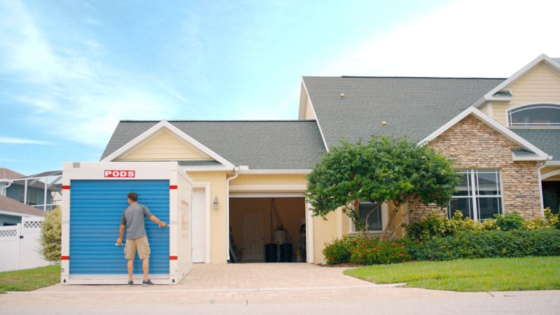 Homeowner opening a PODS moving and storage container in front of a suburban home