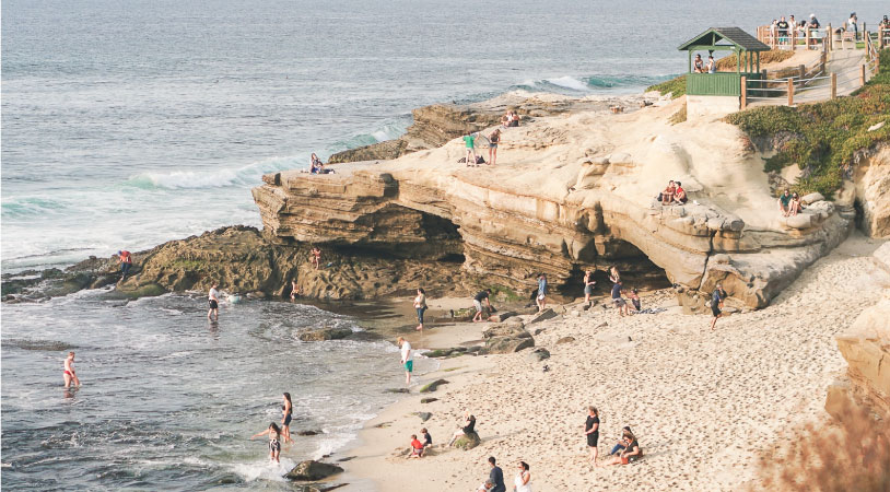 Several beachgoers are enjoying the water and the view from the beach at La Jolla Cove in San Diego.