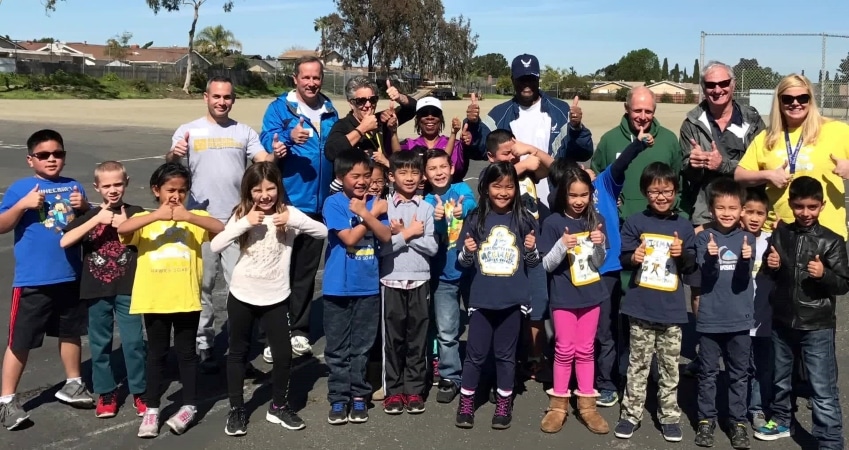 Kids and faculty are all smiling and giving “thumbs up” in a group shot at one of the schools in the San Diego Unified School District.