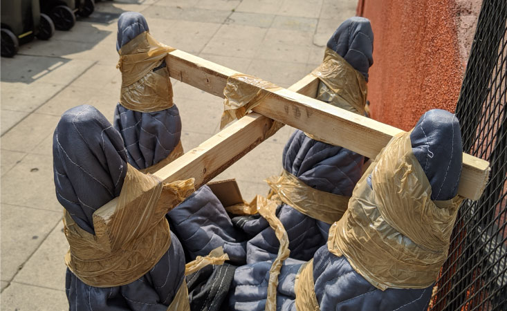 A chair is turned upside down. Its legs are wrapped in a moving blanket and have been secured with stiff wooden planks and tape to prevent damage during a move.