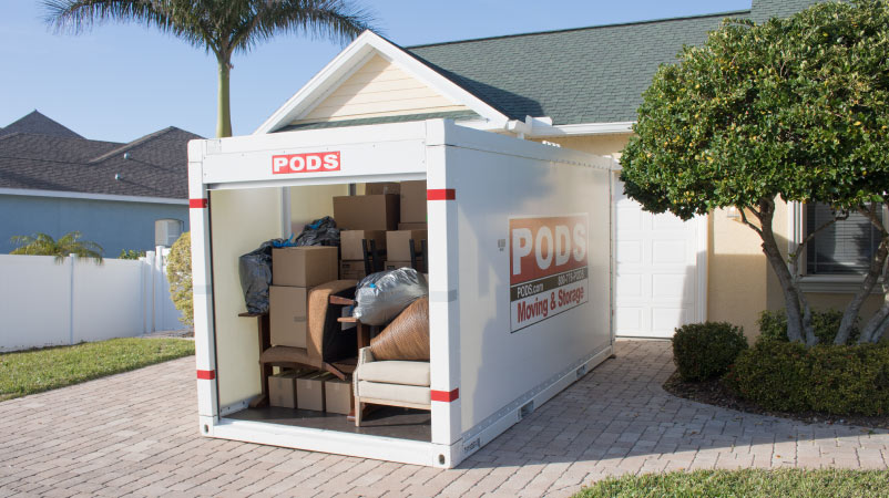 A PODS portable storage container sits in a residential driveway loaded with boxes and furniture.