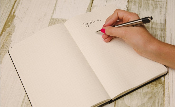 A woman has written “My Plan:” on a fresh page in her notebook. She is preparing to make a strategy for her upcoming move.