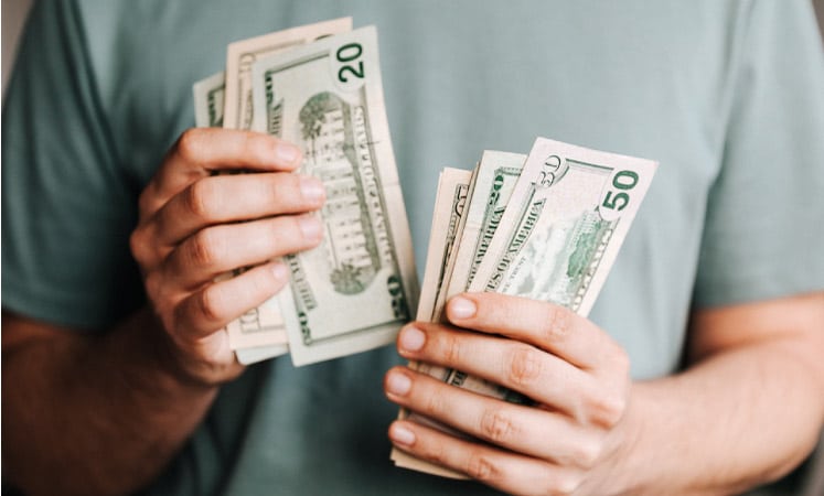 A man in a light blue shirt is counting money. He’s holding several $10, $20, and $50 bills. 