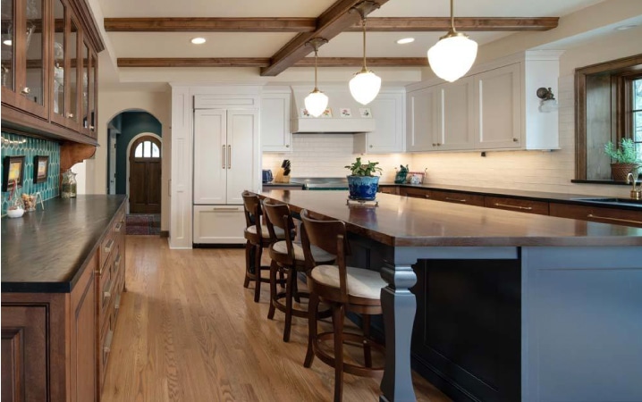 A newly remodeled kitchen with pendant lighting above an island dining table, turquoise-colored tile backsplash, and a combination or white-painted and natural wood cabinets.