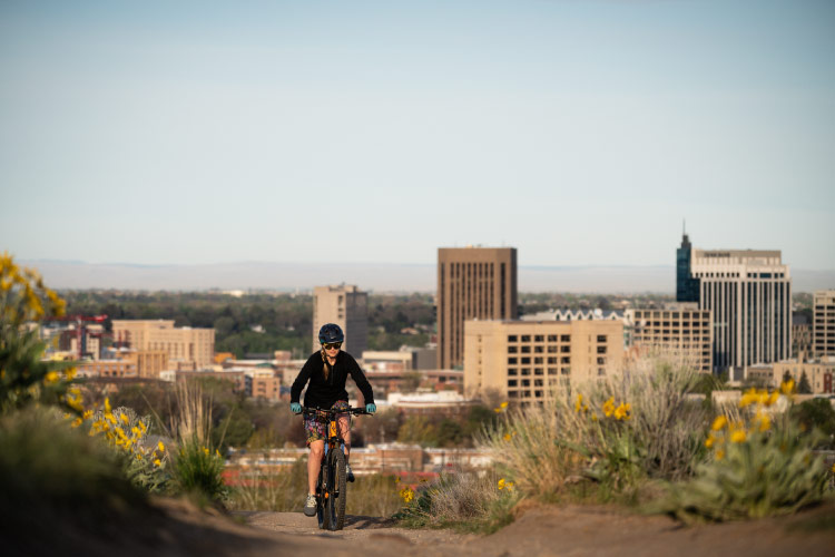 A retired woman rides her mountain bike on the outskirts of Boise, Idaho, with the city skyline behind her. 