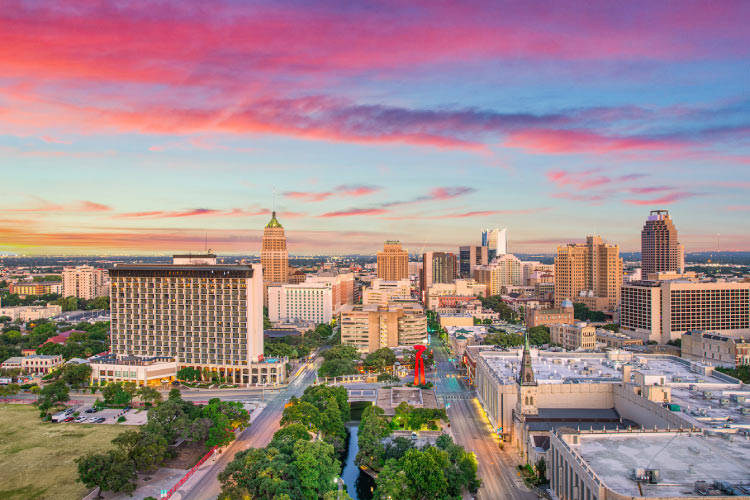 Aerial view of the city of San Antonio, Texas, just before sunset. The sky has wispy clouds in hues of pink and blue. 