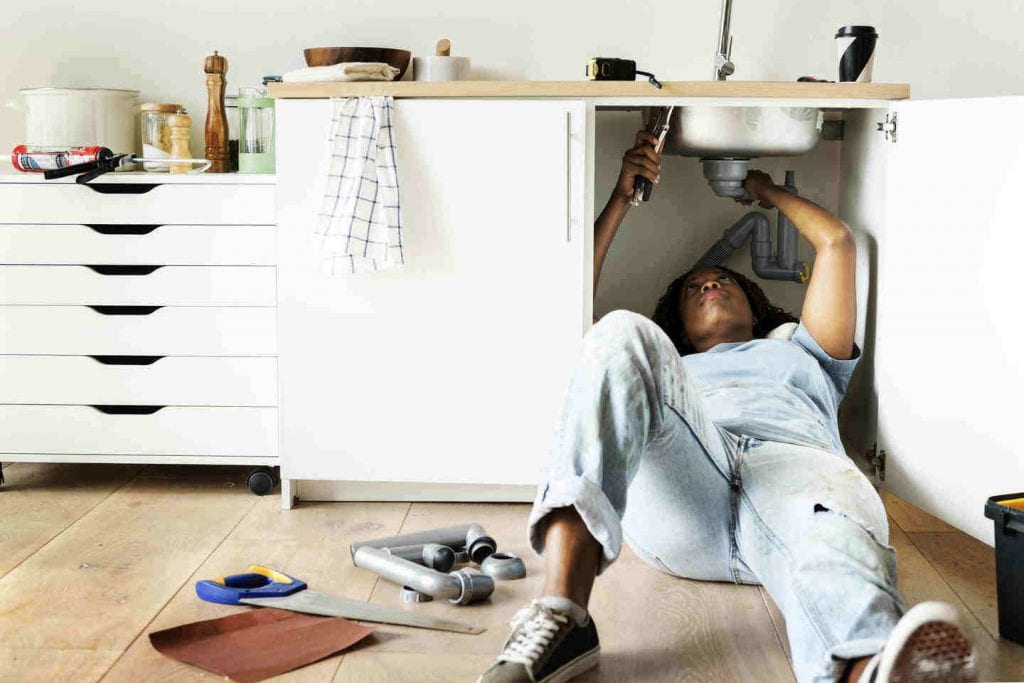 woman adjusting the plumbing under a sink