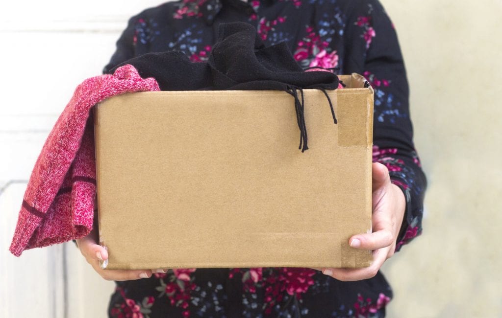 A woman is holding a cardboard box filled with clothing that is ready to be donated.