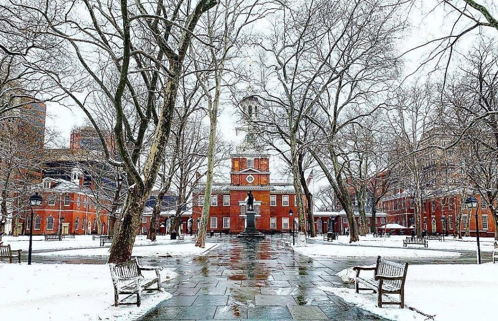 Philadelphia's Independence Hall in the winter. There's snow on the ground, the pathways are wet, and the trees are bare.