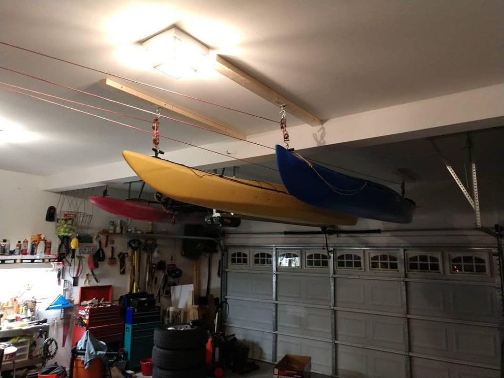Three colorful kayaks secured to a garage ceiling above the garage door. 