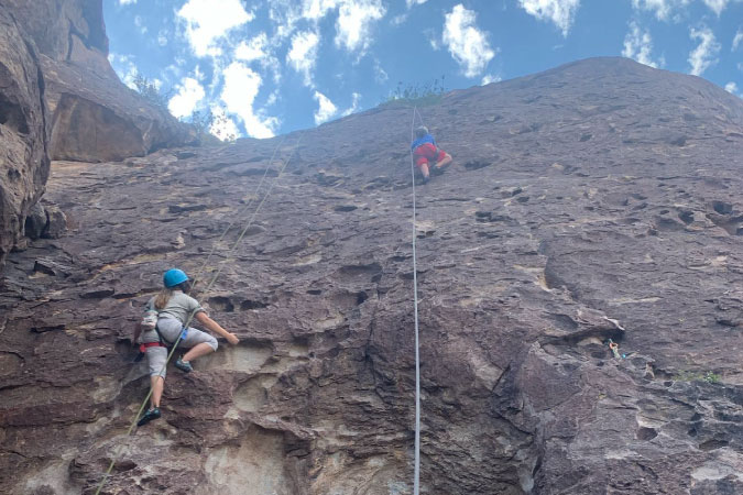 Two young kids climb a natural rock wall in El Paso’s Hueco Tanks State Park.