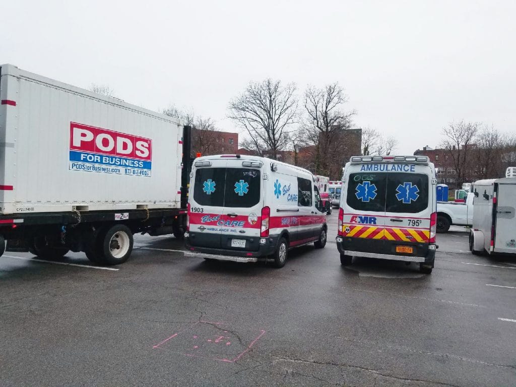 A PODS container on a delivery truck and ambulance vehicles in a hospital lot