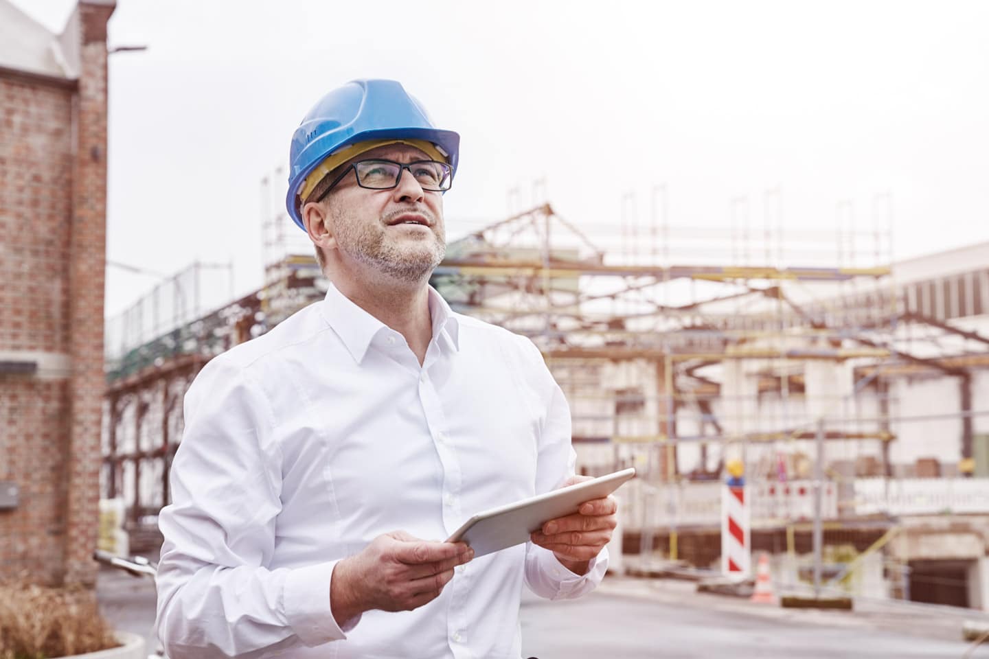 A subcontractor wearing a hardhat reviewing project with a tablet