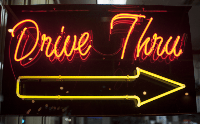 An illuminated neon fast casual restaurant drive thru sign