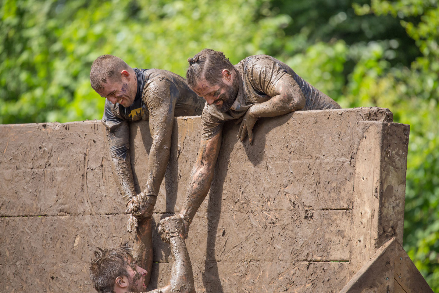 Two men pulling up another man over an obstacle wall at a charity walk or fitness event