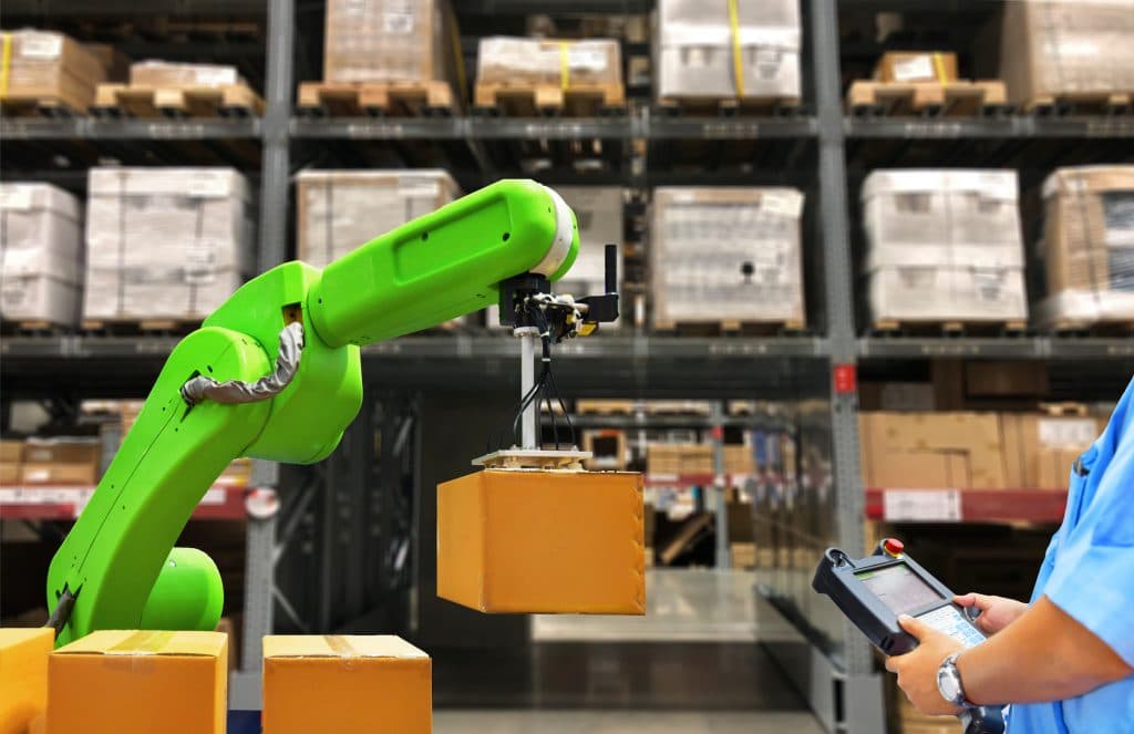 Industrial robot holding a boxs and worker operating a robot machine with a control panel on stock shelves background