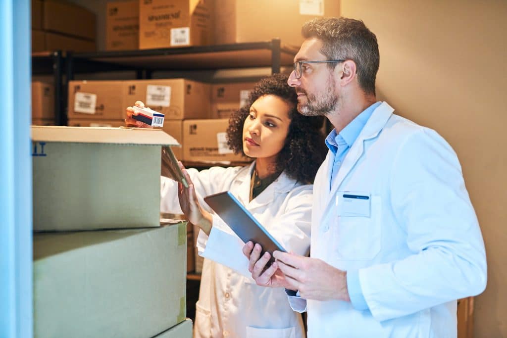 Two medical hospital supply chain professionals  looking at boxes in a warehouse