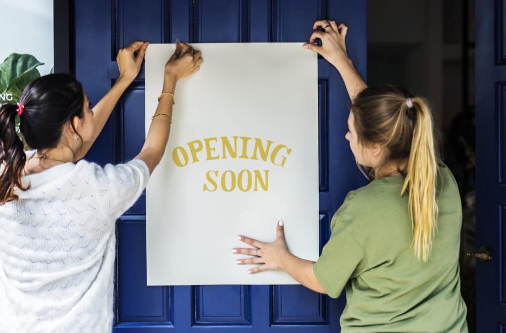 Women hanging an "opening soon" sign on the door of a pop-up hotel