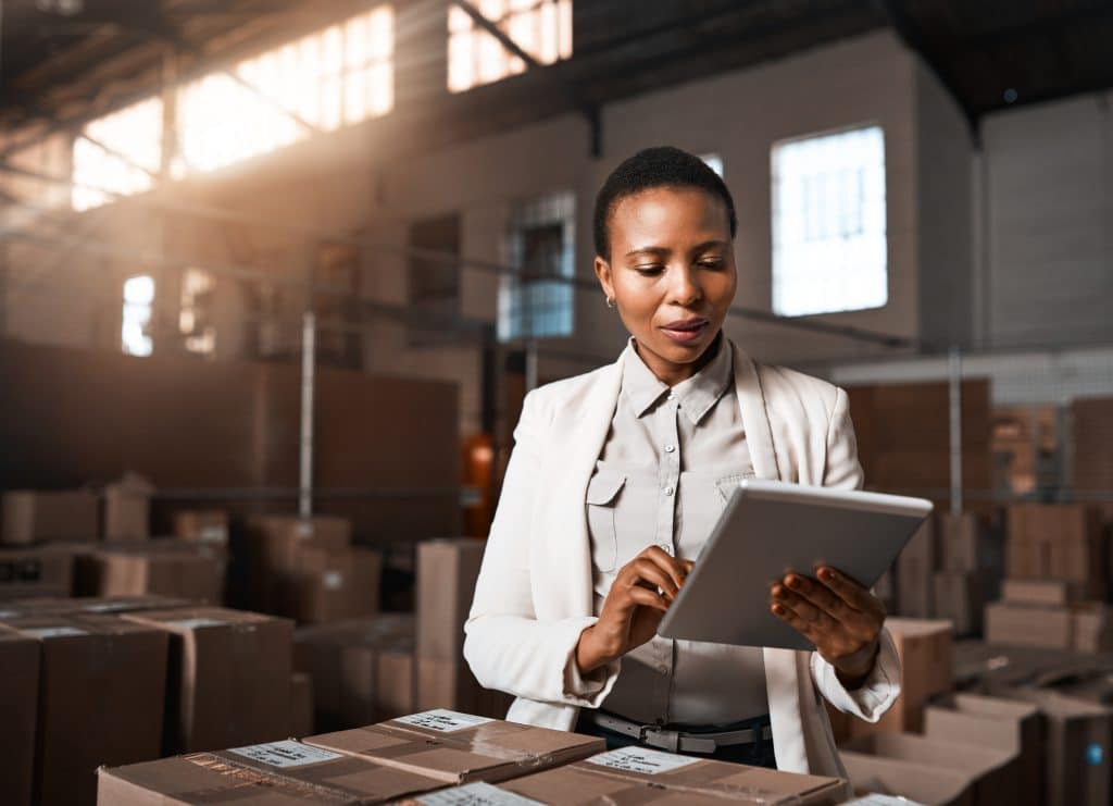 Female employee in a packing warehouse using a tablet to keep track of supply chain data 
