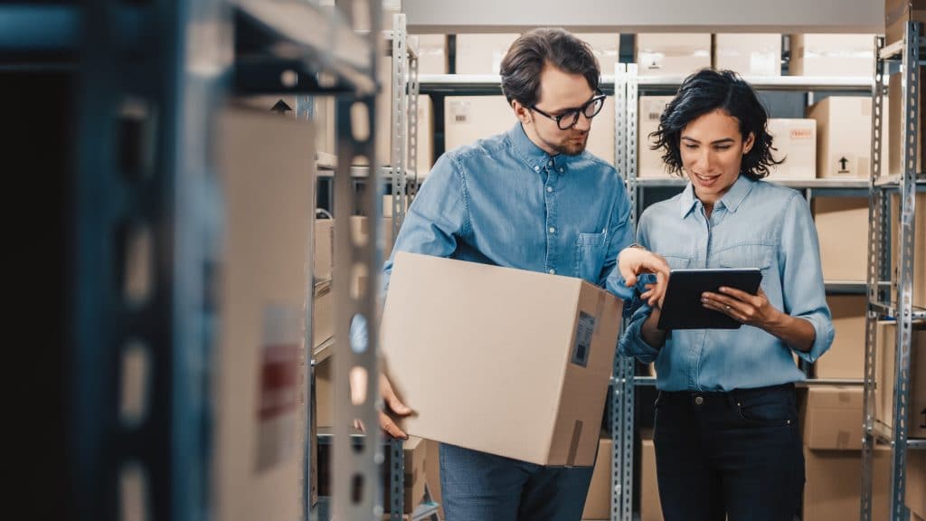 Two employees reviewing inventory on a tablet in a stockroom