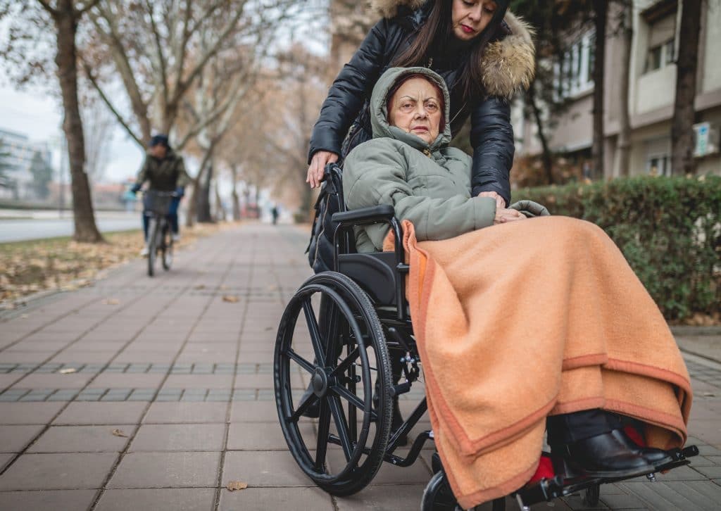 Woman pushing an ailing woman in a wheelchair outdoors in the winter